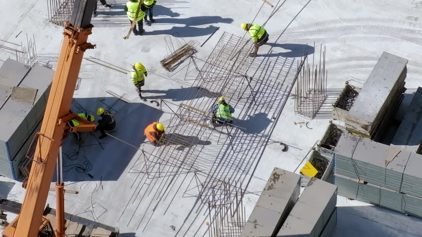 Workers in orange and yellow uniform working with reinforcement and steel bars at the construction site, gray concrete background. Stack of bars around. Top view daylight. High quality FullHD footage Royalty-Free Stock Footage #1101622553