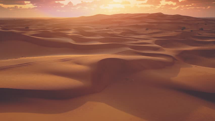 Drone flying over massive sand dunes at sunrise. Aerial bird view of desert landscape. Clouds moving fast in the sky