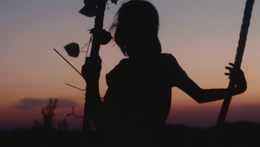 Cinematic silhouette shot, happy carefree teen girl rides swings enjoying late summer sunset sky. Childhood concept.