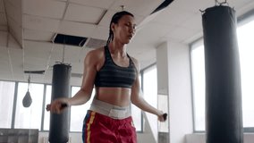 Young asian female boxer with braided hair fast and focused jumping rope next to punching bag warming up before boxing training in the indoor gym - Powered by Shutterstock - Get 15% off with code: PIKWIZARD15
