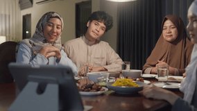 Happy Asian muslim family celebrate long distance with cousin video call online Ramadan dinner together in dining room at home. Two generation celebration end of Eid al-Fitr togetherness at home.