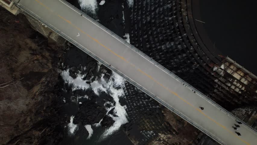 An aerial view high over the waterfalls at the Croton Gorge dam in upstate New York during a cloudy winter day. The drone camera tilted down dolly out then tilt up over the bridge and waters.