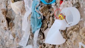 Vertical video, Close-up of disposable plastic, face mask and other debris on corals beach in surf zone. Plastic and other garbage on the seashore. Slow motion