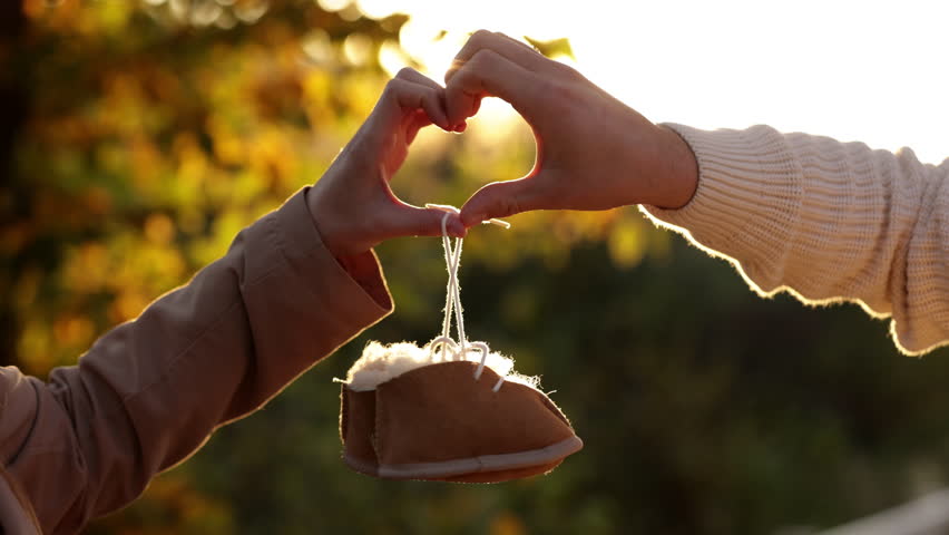 Man and pregnant wife are doing heart gesture with hands and holding warm baby shoes on nature autumn background. Future parents waiting for the baby. The concept of Mother's Day and Women's Day Royalty-Free Stock Footage #1101635019