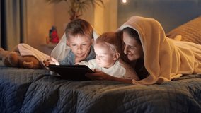 Happy family relaxing in bed with tablet computer. Family having time together, parenting, happy childhood and entertainment.