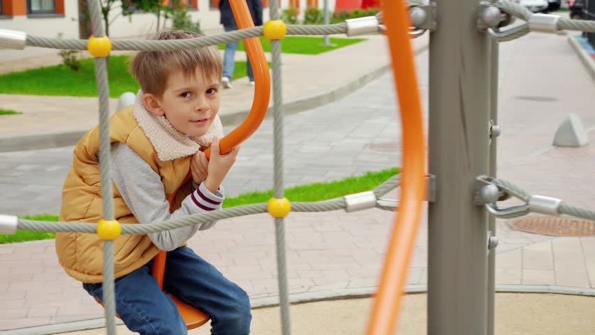 Cute smiling boy holding tight as he spins on merry go round carousel at public playground. Active child, sports and development, kids playing outdoors.