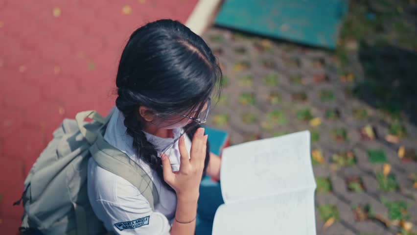 An overhead shot of a diligent young student reading a book or notebook while sitting on a bench outdoors. This clip is ideal for concepts of academic dedication, focus, and quiet study time.