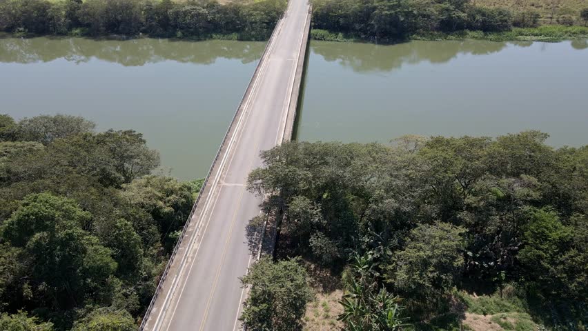 Old beetle green car traveling passing by the bridge over the river aerial view in a sunny day with sun reflexion
