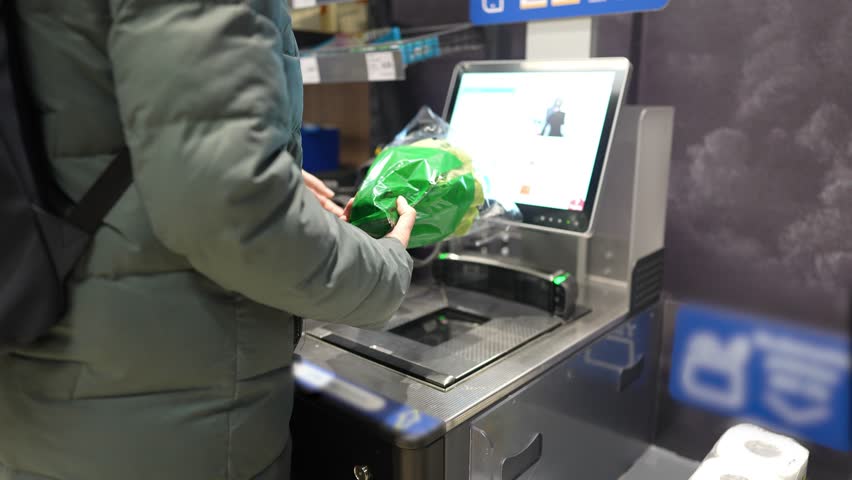 The girl scans the goods at the self-service checkout and pays for the purchase using the phone | Shutterstock HD Video #1101640029