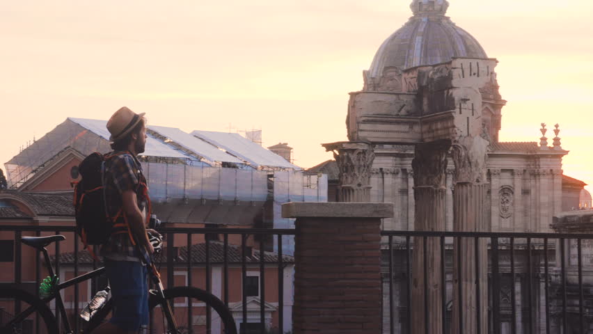 Young man tourist with backpack and bike walking at Roman Forum at sunrise. Historical imperial Foro Romano in Rome, Italy from panoramic point of view. Royalty-Free Stock Footage #1101641133