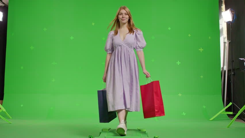 Attractive red-haired white girl walks to the side against the background of a green screen. Happy young woman walking with shopping bags on a Green Screen, Chroma Key