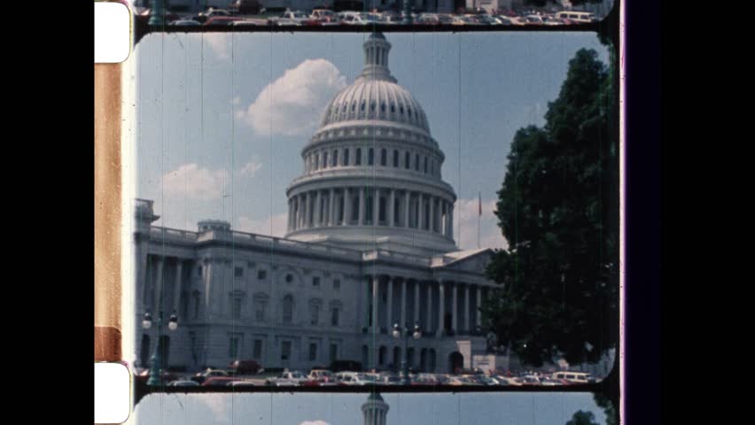 1985 Washington, DC. Politicians ascend the steps of the Capitol Building. Slow zoom out to reveal the Capitol dome. Scratched emulsion, dusty particles on grainy footage. 4K Overscan of archival film