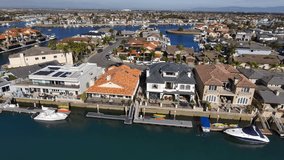 backwards aerial footage the still blue waters of Huntington Harbour surrounded by homes and lush green palm trees with blue sky and clouds in Huntington Beach California USA
