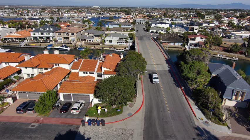 aerial footage the still blue waters of Huntington Harbour surrounded by homes and lush green palm trees with blue sky and clouds in Huntington Beach California USA