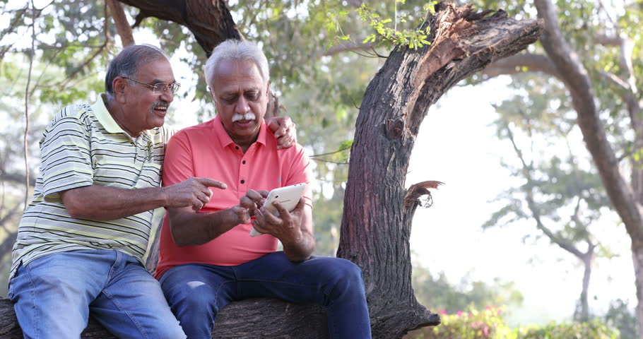 Two senior male friends using digital tablet at park.