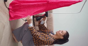 Vertical video of a young woman is steaming a long red dress. Preparing a summer dress for going out after washing. Close-up 4k footage.