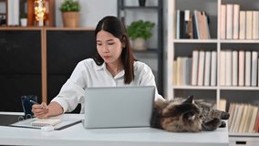 Asian woman entrepreneur working online from home, using laptop computer and making notes on notebook
