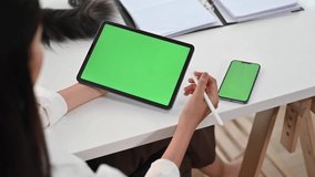 Above view of young woman freelancer using digital tablet, holding stylus pen scrolling on green screen