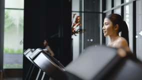 Young asian girl jogging on a treadmill in a gym, close-up, side view, Muscular athletes actively training in the gym, Female training at fitness center. Woman exercising cardio workout