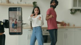 Funny couple dancing to popular music having fun in kitchen recording self video dance on mobile phone camera for social media multiracial indian arabian man woman dancers bloggers record trend move