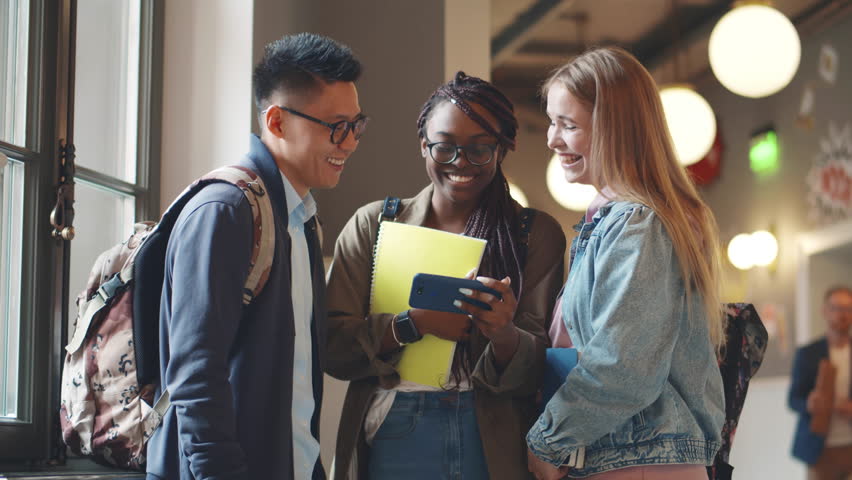 Multiethnic young college students using smartphone in corridor. Diverse friends look at cellphone and laugh in university hallway. Man and women use mobile phone together. Realtime - Powered by Shutterstock - Get 15% off with code: PIKWIZARD15