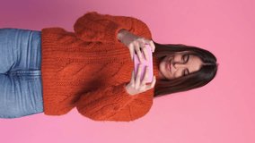 Smiling woman in sweater playing mobile games in studio. Vertical video.