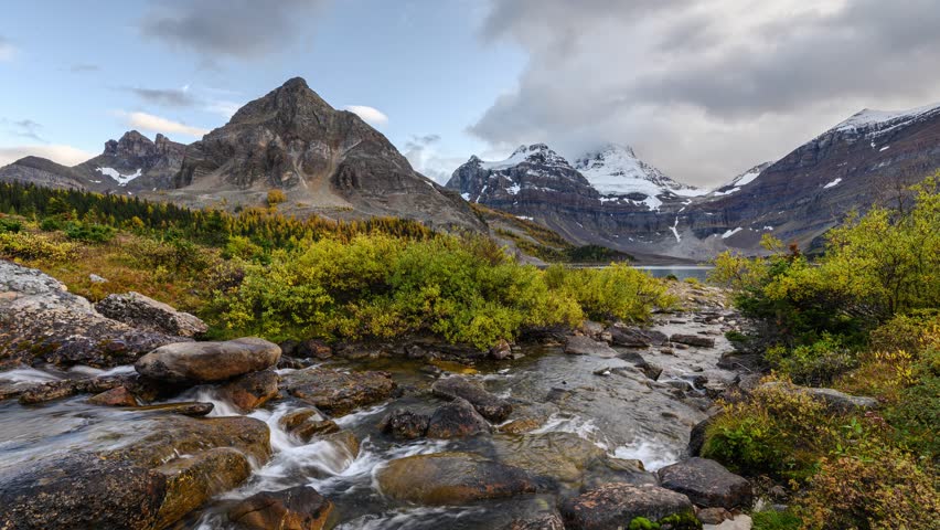 Time lapse scenery of Mount Assiniboine with stream flowing to Lake Magog in autumn forest on sunny day at Assiniboine provincial park, BC, Canada