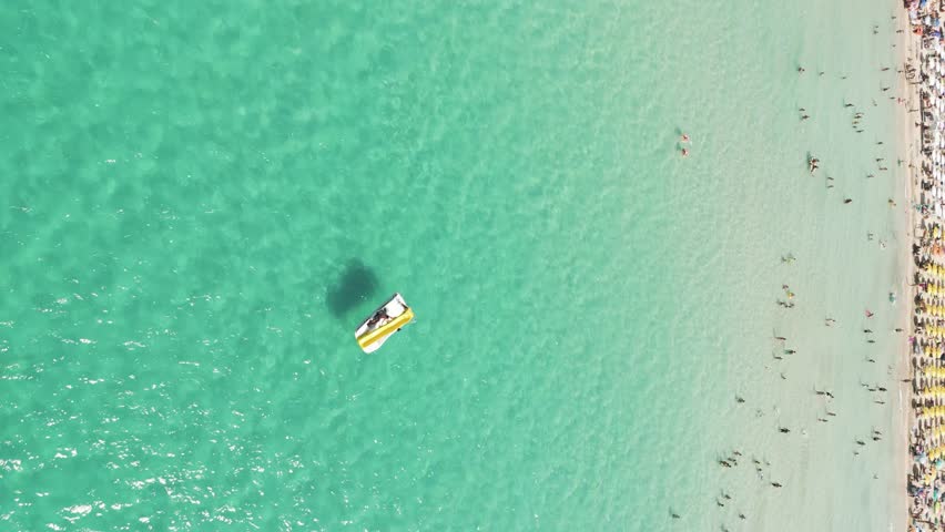 Vertical aerial view of people on a pedal boat along the shoreline in summertime in Sicily, Italy.