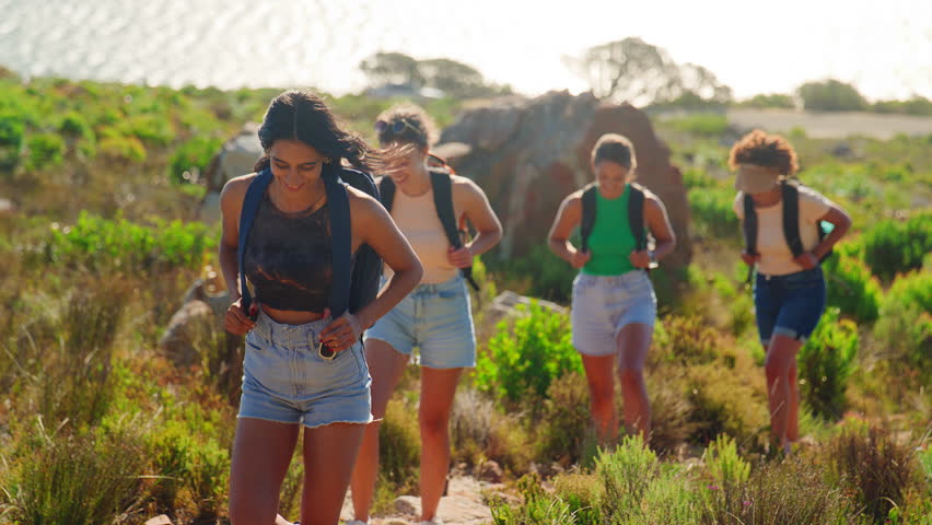 Group of female friends with backpacks on hiking vacation in countryside along coastal path - shot in slow motion Royalty-Free Stock Footage #1101666179