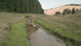 Aerial cinematic footage from FPV racing drone of a creek during a partly cloudy summer day. Flying above the stream in between electric poles. Cierny Balog, Slovakia. LuPa Creative.
