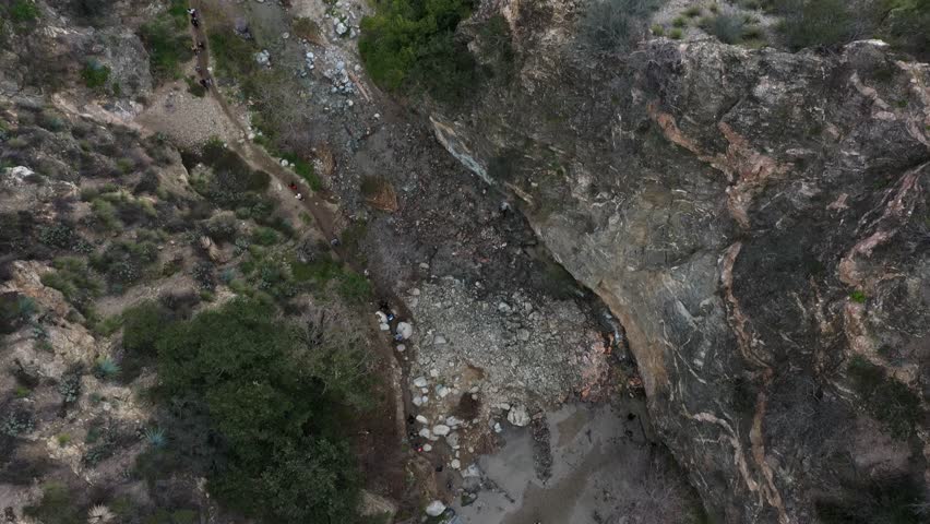Several hikers walking through Eaton Canyon Falls trail in Pasadena, Angeles National Forest, California. Aerial dolly tilt.
