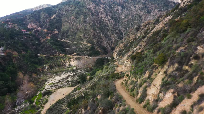 Mt. Wilson toll road pushing towards Chuck Ballard Memorial Bridge and Eaton Canyon hikers hiking. Aerial dolly tilt.