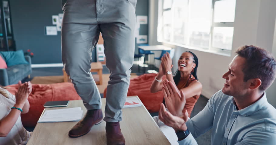 Businessman, dancing and table with happy team in applause for celebration, achievement or goal at the office. Employee man celebrating with fun dance on desk with colleagues clapping at workplace