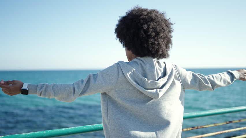 African american woman wearing sportswear stretching arms at seaside