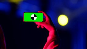 Man's hand holds phone with chromakey, shooting video at party, mockup. Concept of concert, party and holiday