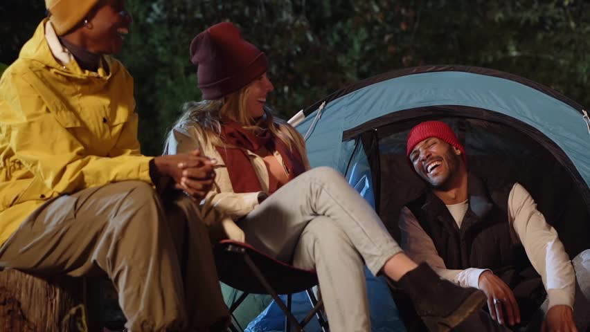 Multiracial boys and girls chatting and smiling amused at a winter camping trip. Young adults gathered outdoors in the evening at the campsite. Group of happy people at the vacation camp. Royalty-Free Stock Footage #1101675649