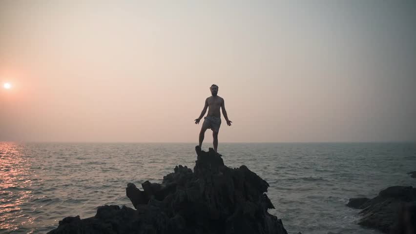 A man stands on a slip during sunset and gently raises his hands.