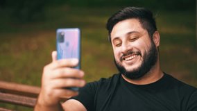 A young man smiling communicates outdoors via video call on a smart phone close-up shot