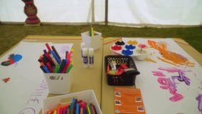 stationery kids painting drawing workshop inside tent with pencils, multi coloured pencils and wet painting nobody around empty drawings on paper everything looking neat moving motion scene festival