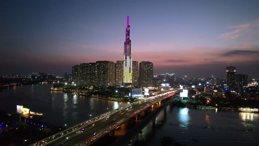 Aerial View of Ho Chi Minh City and Slow Flying Towards Illuminated Landmark 81 Super Tall Skyscraper at colorful Sunset in Vietnam, Night Traffic on Saigon Bridge Royalty-Free Stock Footage #1101692417