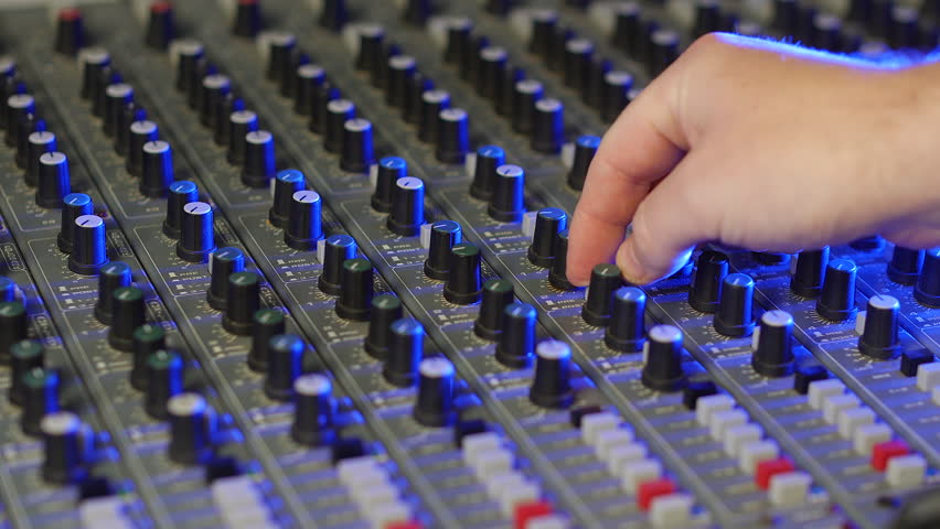 A sound engineer music producer adjusting the audio on a mixing desk turning the knobs and pressing buttons | Shutterstock HD Video #1101699973