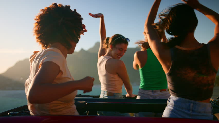 Rear view of female friends standing up through sunroof of car laughing on road trip through countryside with friends - shot in slow motion Royalty-Free Stock Footage #1101700113