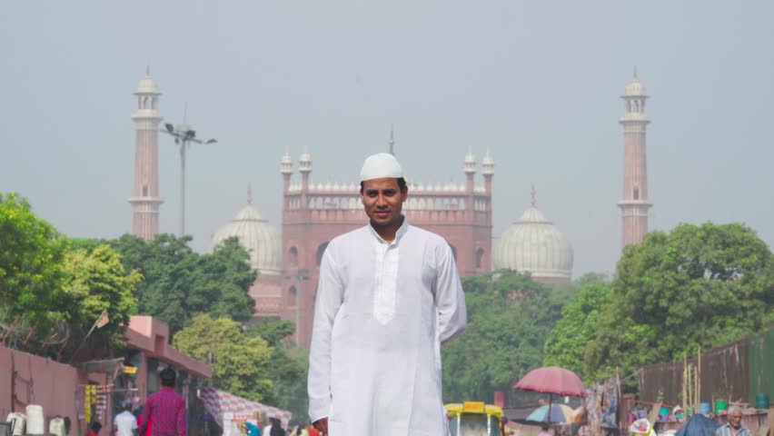 Indian muslim man doing adab to the camera in front of a mosque