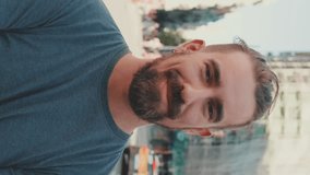 VERTICAL VIDEO, Close-up of young smiling man with beard standing in front of busy intersection