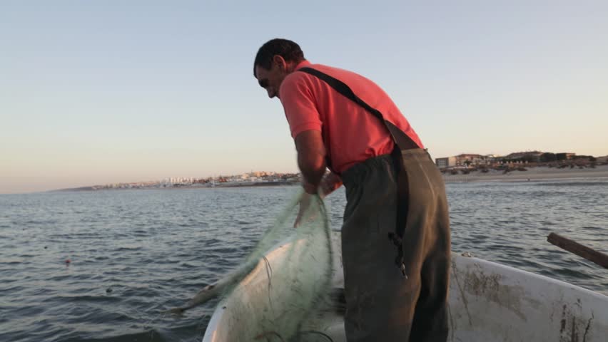 Fisherman in a boat collecting net from the sea during sunrise