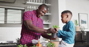 Video of happy african american father and son planting flowers at home. Family, spending quality time together at home concept.