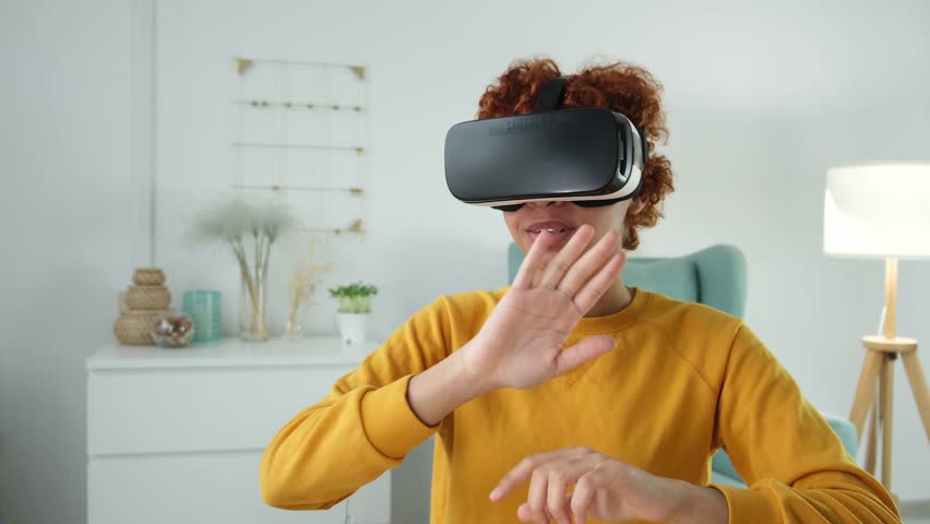 African american young woman wearing using virtual reality metaverse VR glasses headset at home. Girl touching air during VR experience on virtual reality helmet. Simulation hi-tech videogame concept Royalty-Free Stock Footage #1101705185