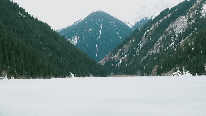 Girl hiker with Backpacklooking around on the ice lake with mountains. High quality FullHD footage
