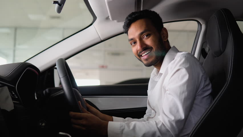 Portrait of a happy indian man driving a new luxury electric car in a car dealership. The man shows emotions of happiness while driving in his new car. Right hand drive car Royalty-Free Stock Footage #1101708941