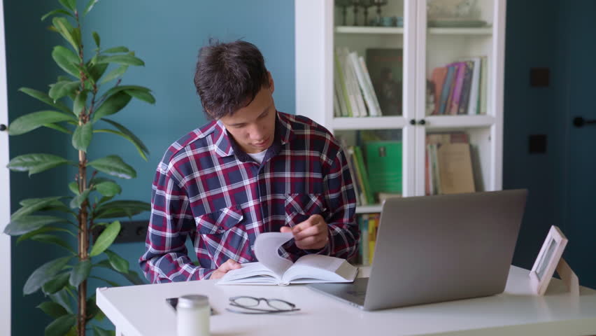 Young biracial man student studying at home looking for information in book, using laptop computer online self education discipline doing creative coursework research homework assignment sit at desk Royalty-Free Stock Footage #1101713033